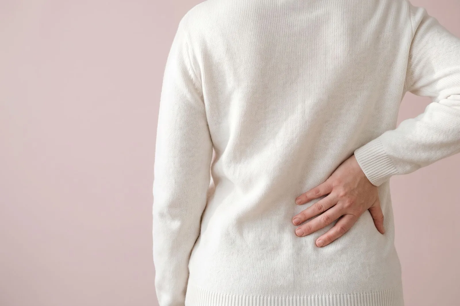 A hand resting on the lower back over a jumper